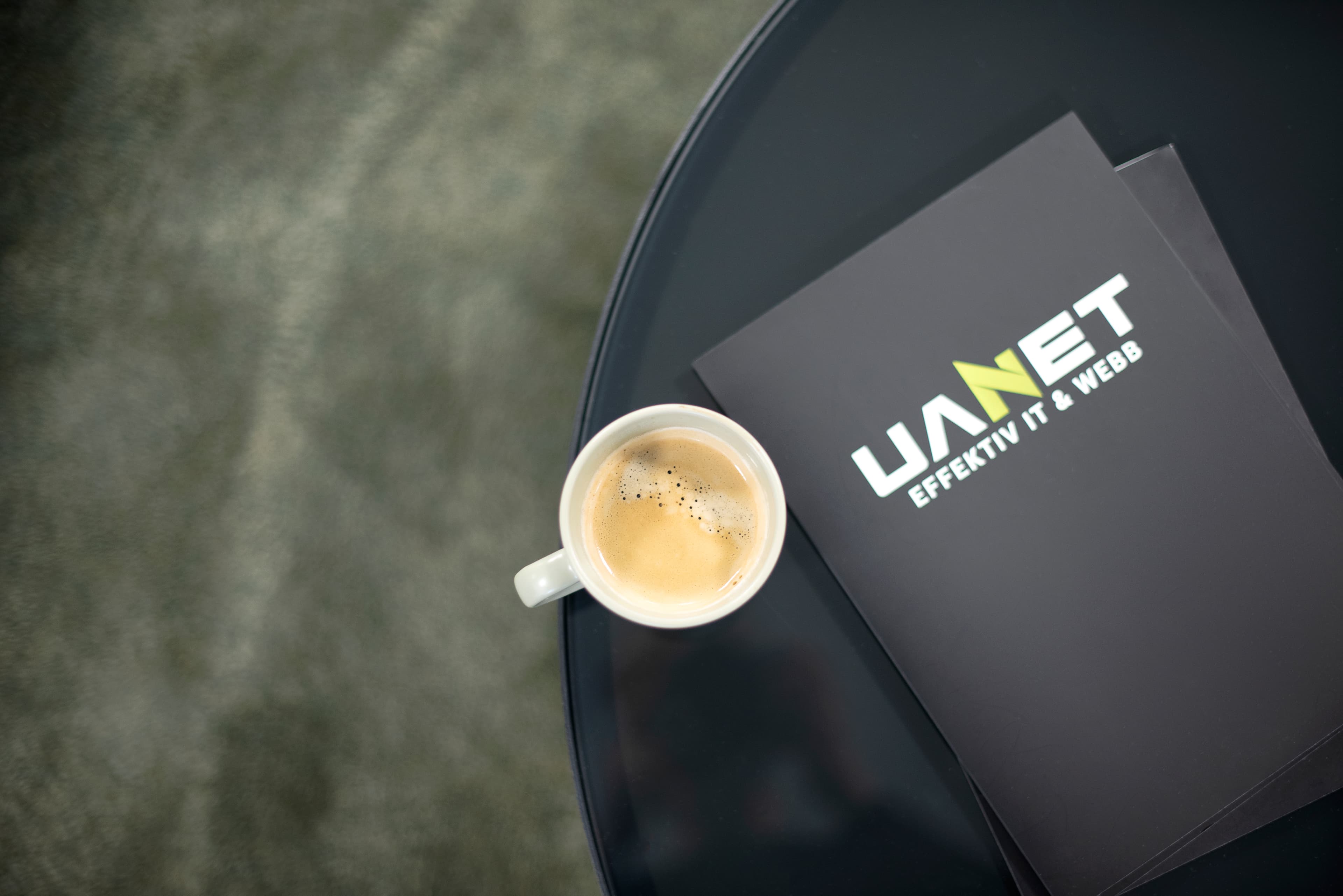 En kaffekopp och en broschyr med UANETs logotyp på ett bord